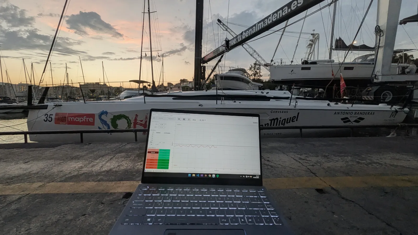 HeelMetrics en un portátil frente a un velero, al atardecer en el puerto